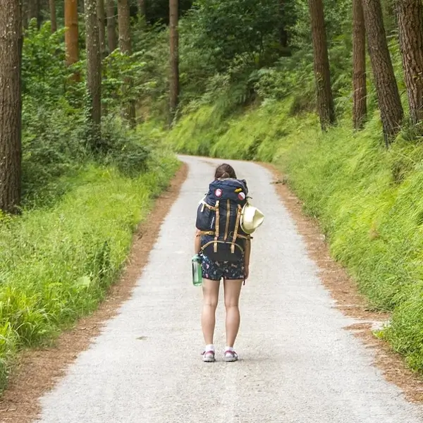 Une jeune femme avec un sac à dos marche sur un sentier en pleine nature.