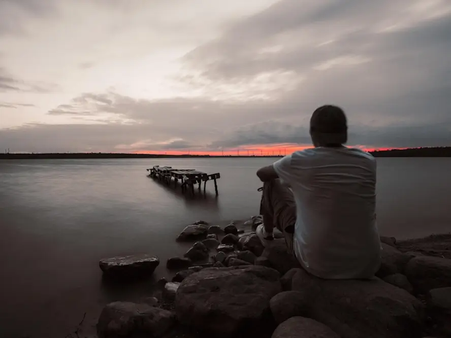 Une homme assis parterre devant un grand lac