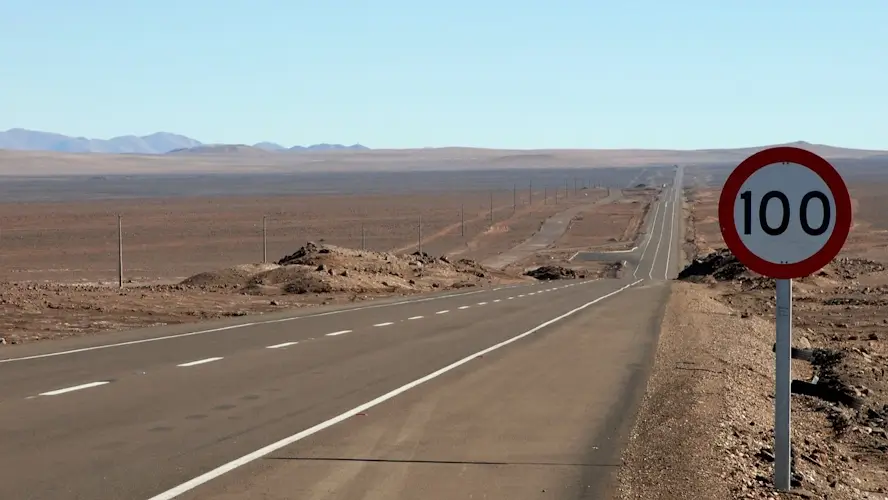 Un panneau de limite de vitesse devant une longue route