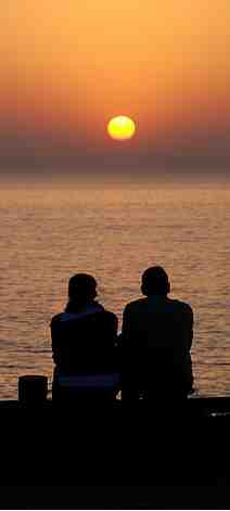 Deux amoureux, l’un près de l’autre, contemplent un coucher de soleil.