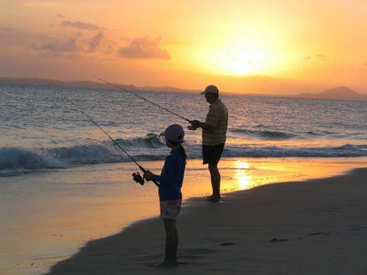 Deux pêcheurs avec leurs lignes à la mer devant un coucher de soleil.