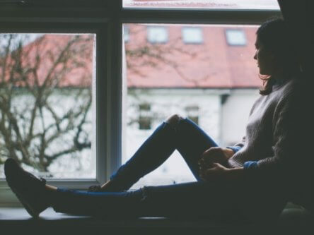 Une jeune femme triste assise près d’une fenêtre