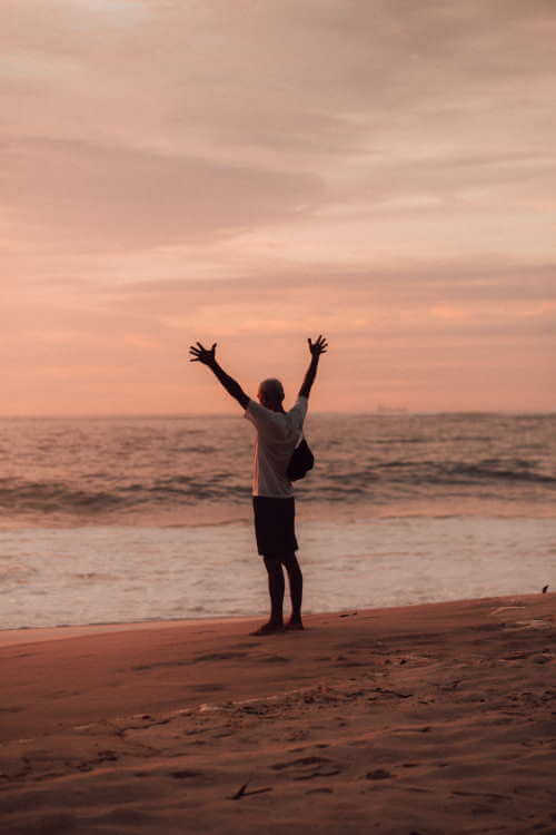 Un homme les bras en l’air devant la mer.