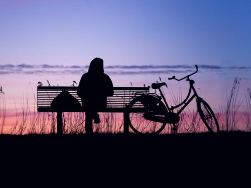 Une personnes est assise sur un banc de parc près d’une vélo.