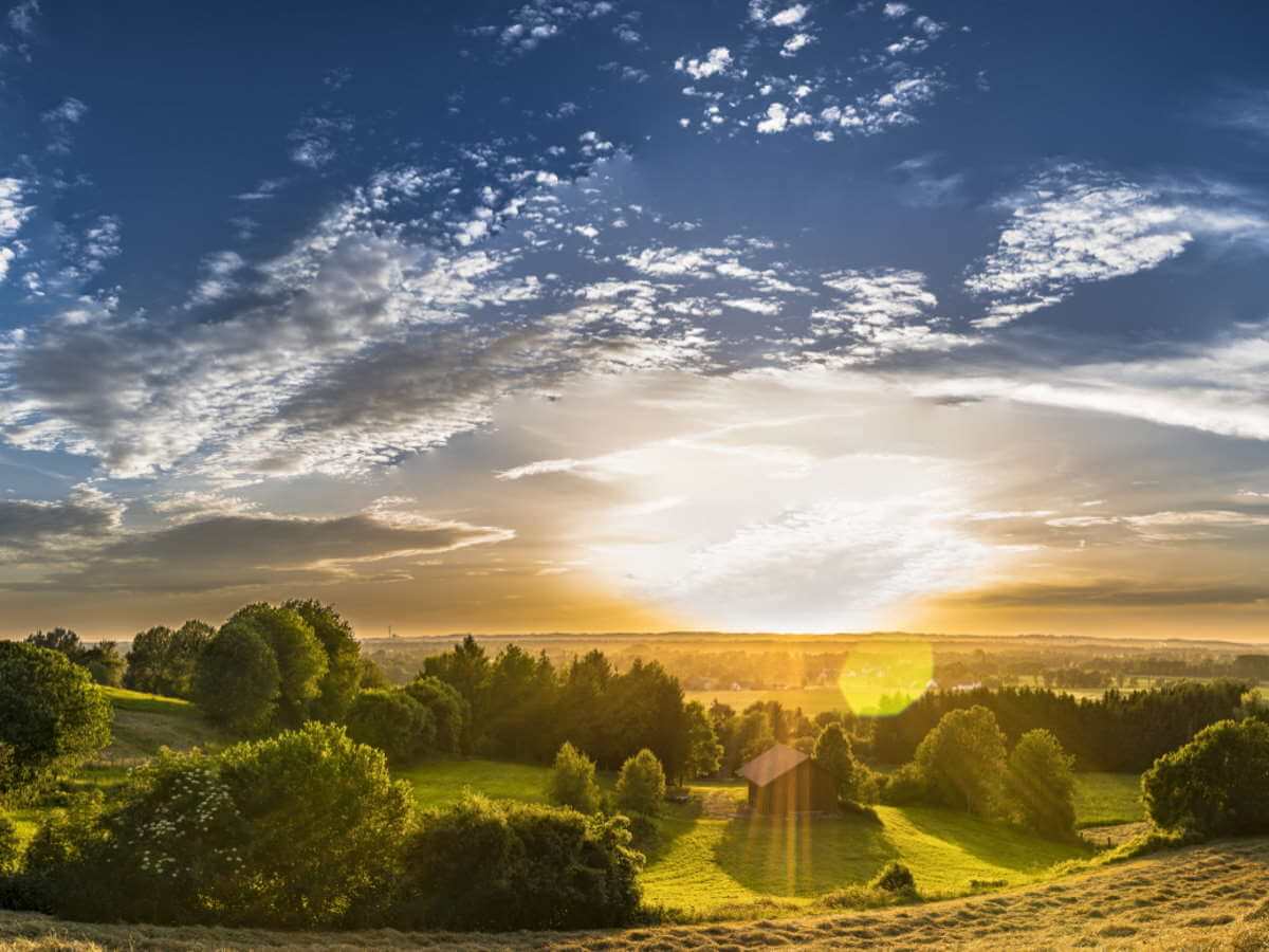 Lever de soleil sur une vallée de champs et d’arbustes.