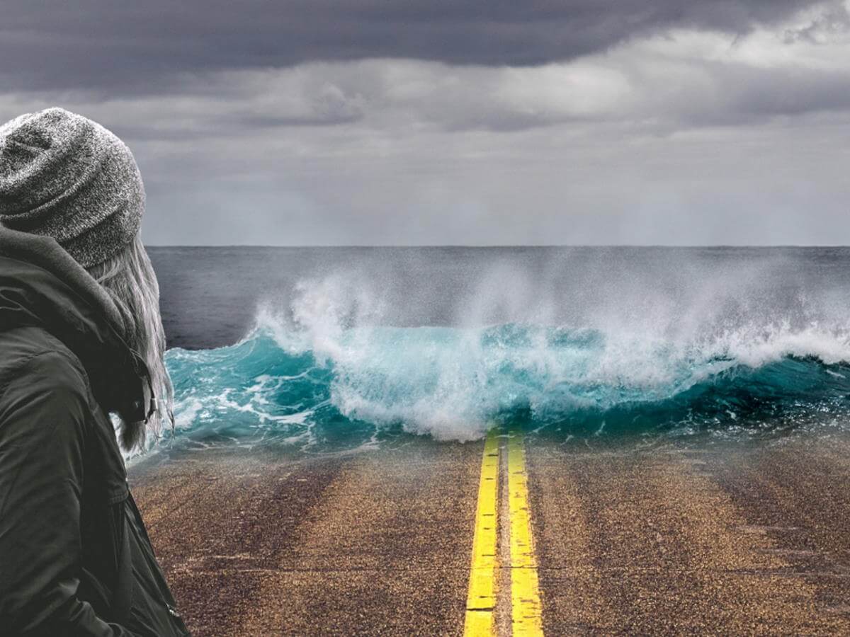 Une jeune dame devant une grosse vague qui vient vers elle.