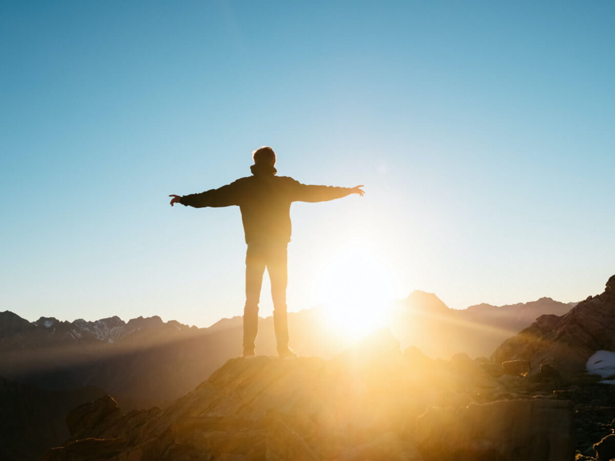 Un homme au sommet d’une montage devant le soleil
