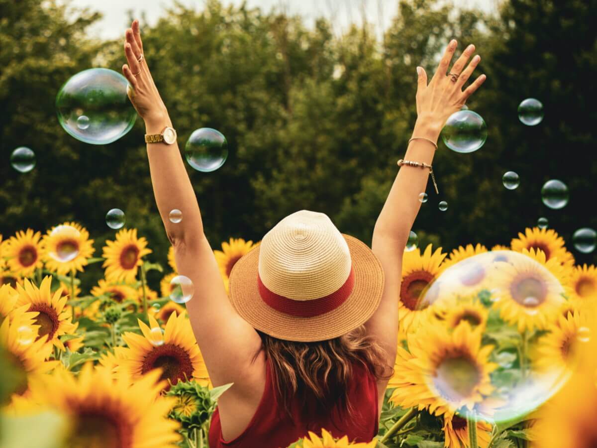 Une dame lève les bras vers le ciel dans un champ de fleurs.