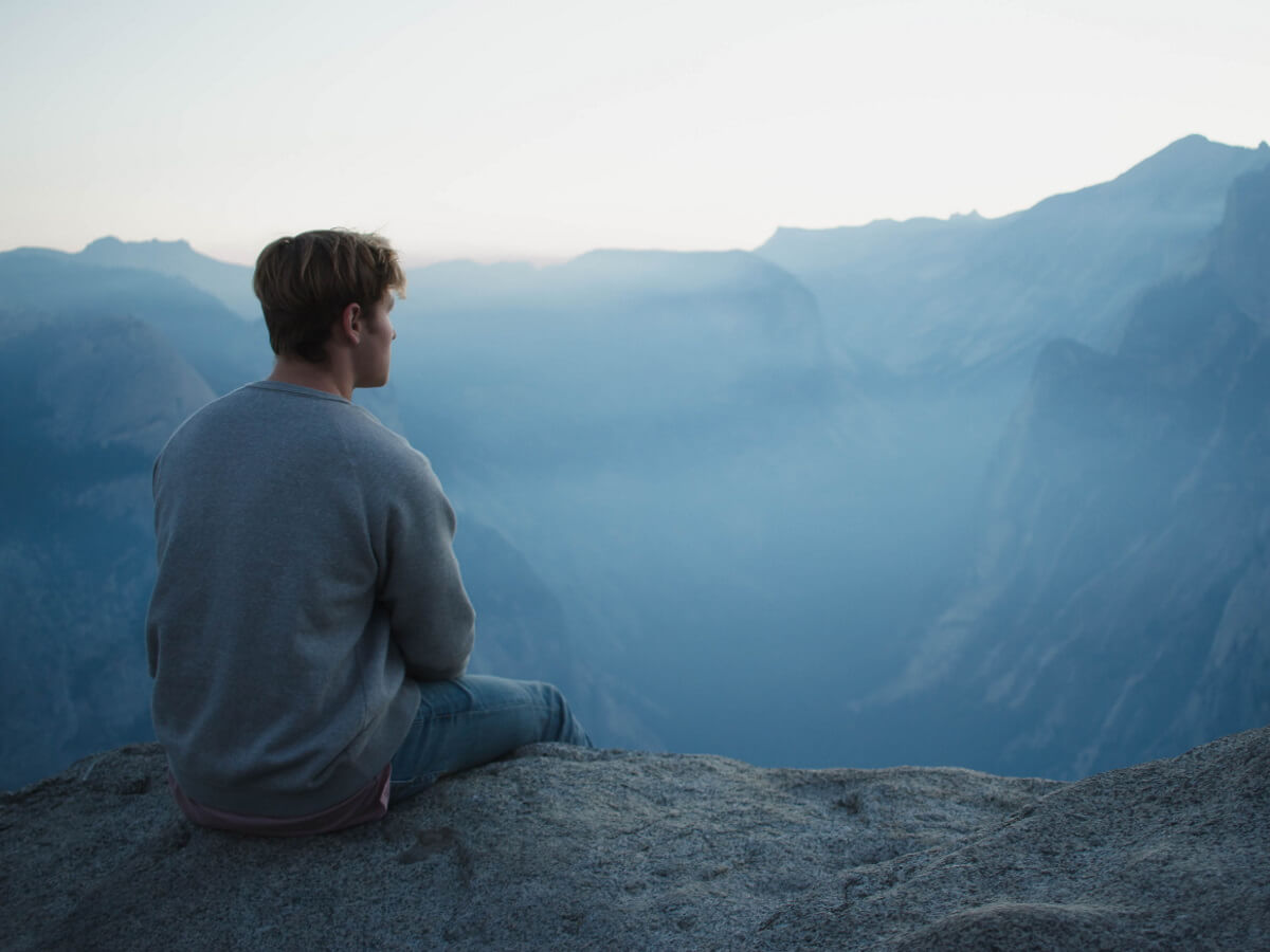 Un homme assis devant un paysage montagneux.