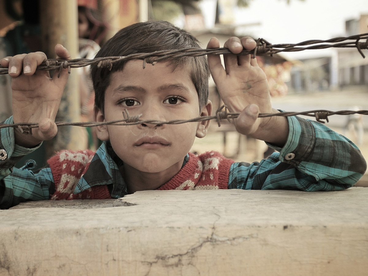 Un enfant triste derrière des barbelés.