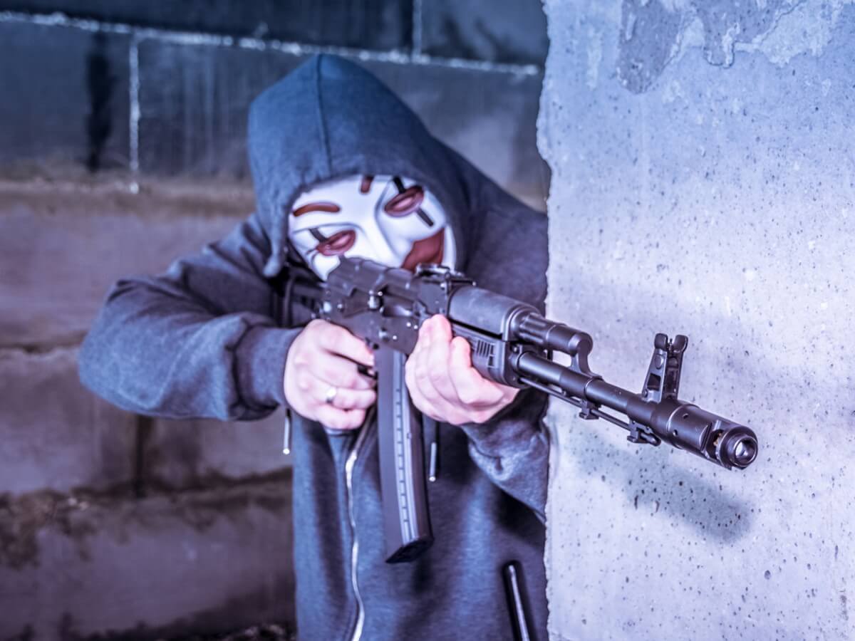 Un homme masqué pointe une mitraillette.