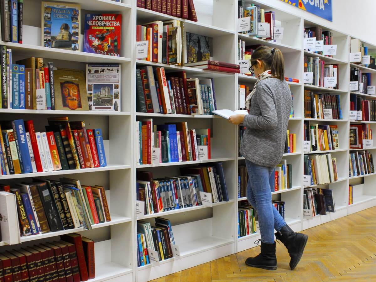 Une jeune femme cherche devant une bibliothèque de livres.