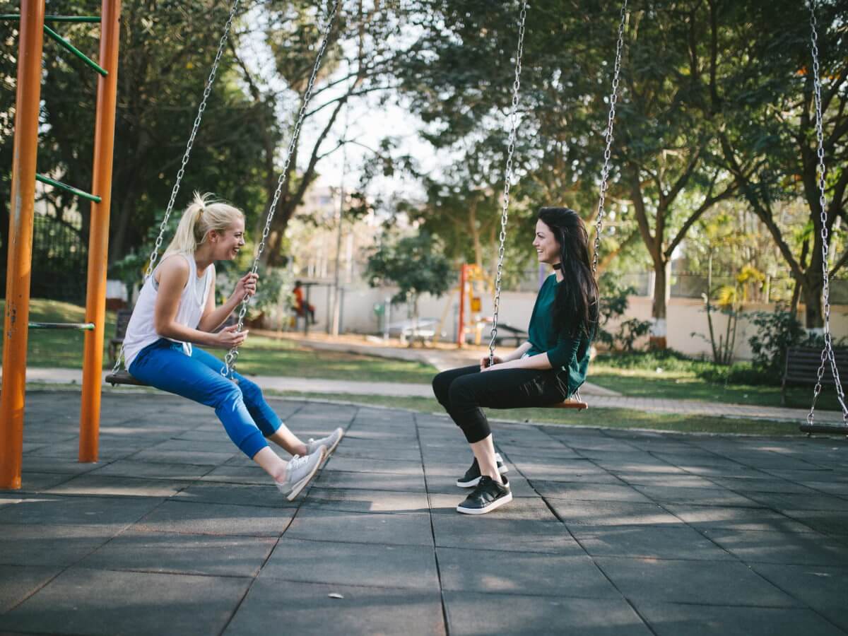 Deux jeunes dames rigolent assises dans un terrain de jeu.