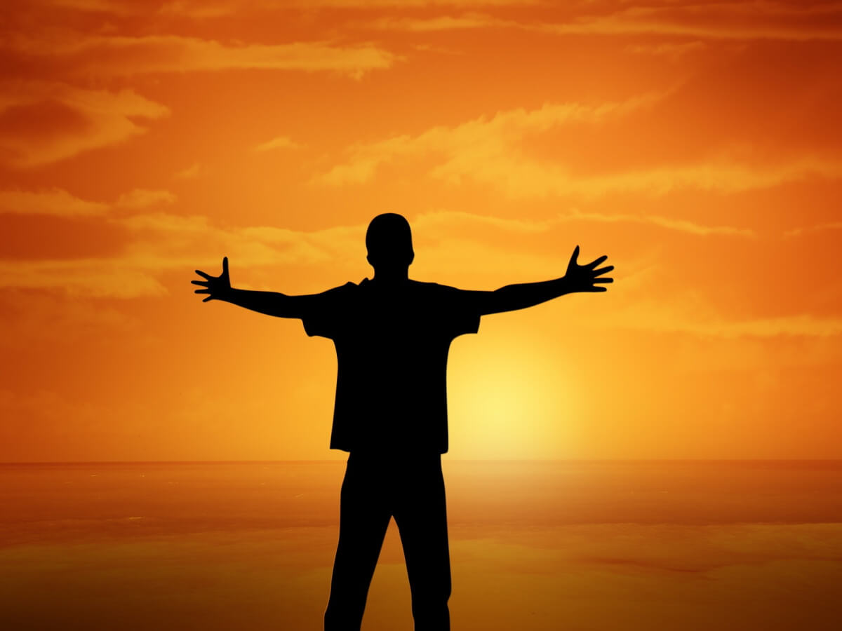 Un homme a les bras ouverts devant un lever de soleil.