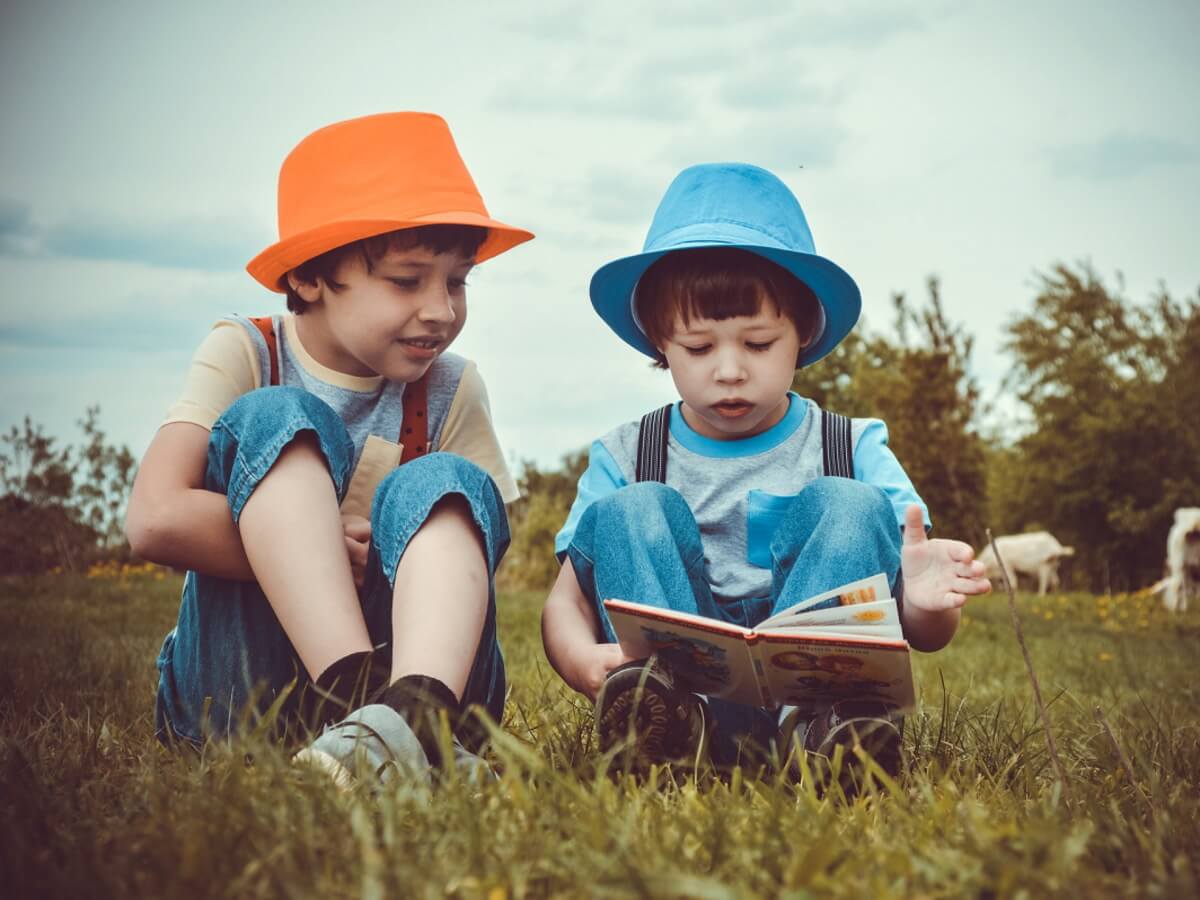 Deux-garçons en train de lire assis sur l’herbe.