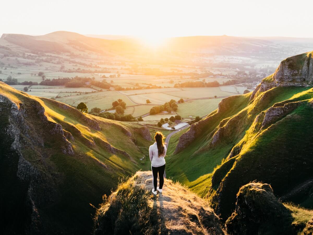 Une dame regarde le soleil se lever sur une vallée verdoyante.