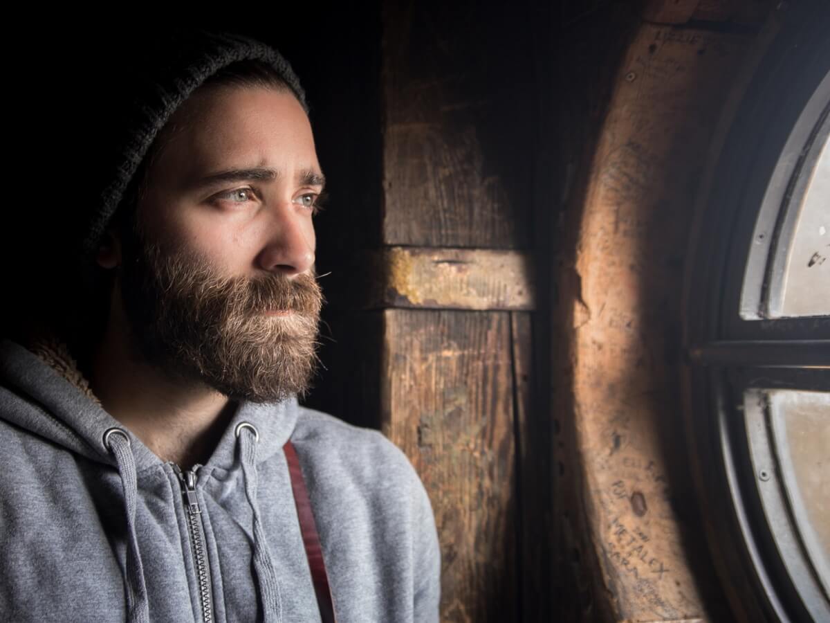 Un jeune homme triste regarde par la fenêtre.