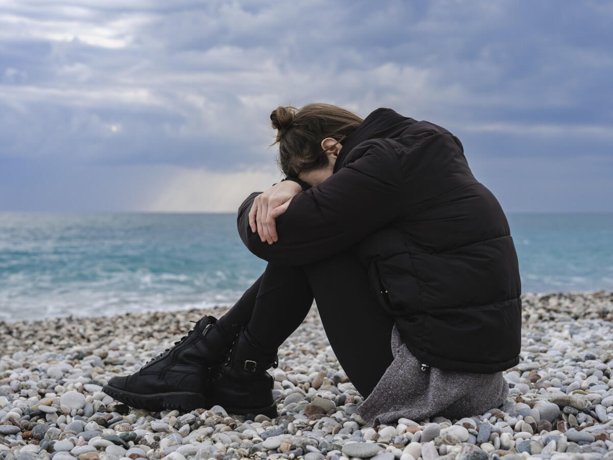 Une femme près de la mer baisse la tête.