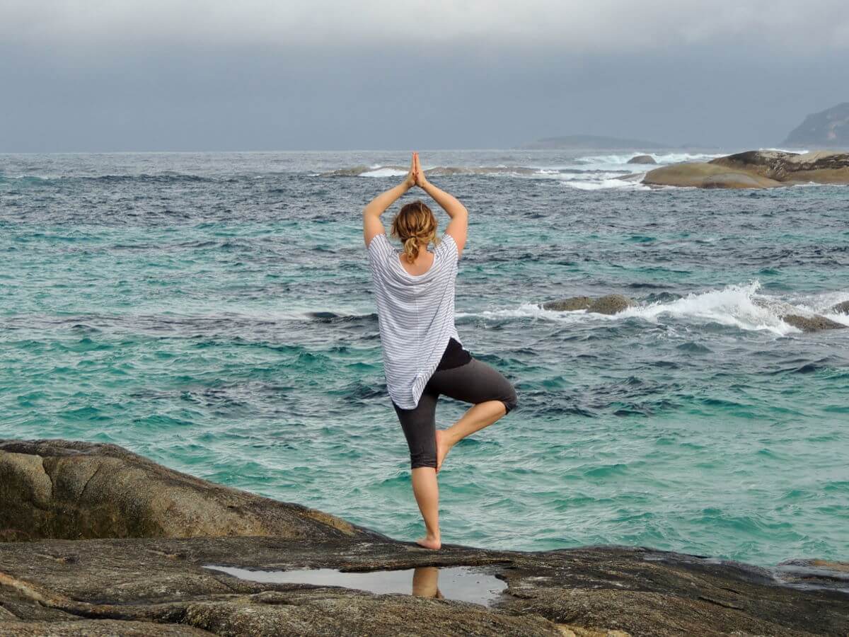 Une dame fait du yoga sur la plage.