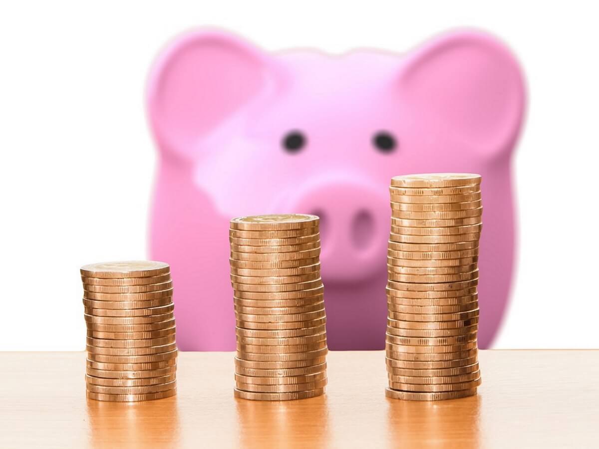 Des pièces de monnaie devant une tirelire en forme de cochon.