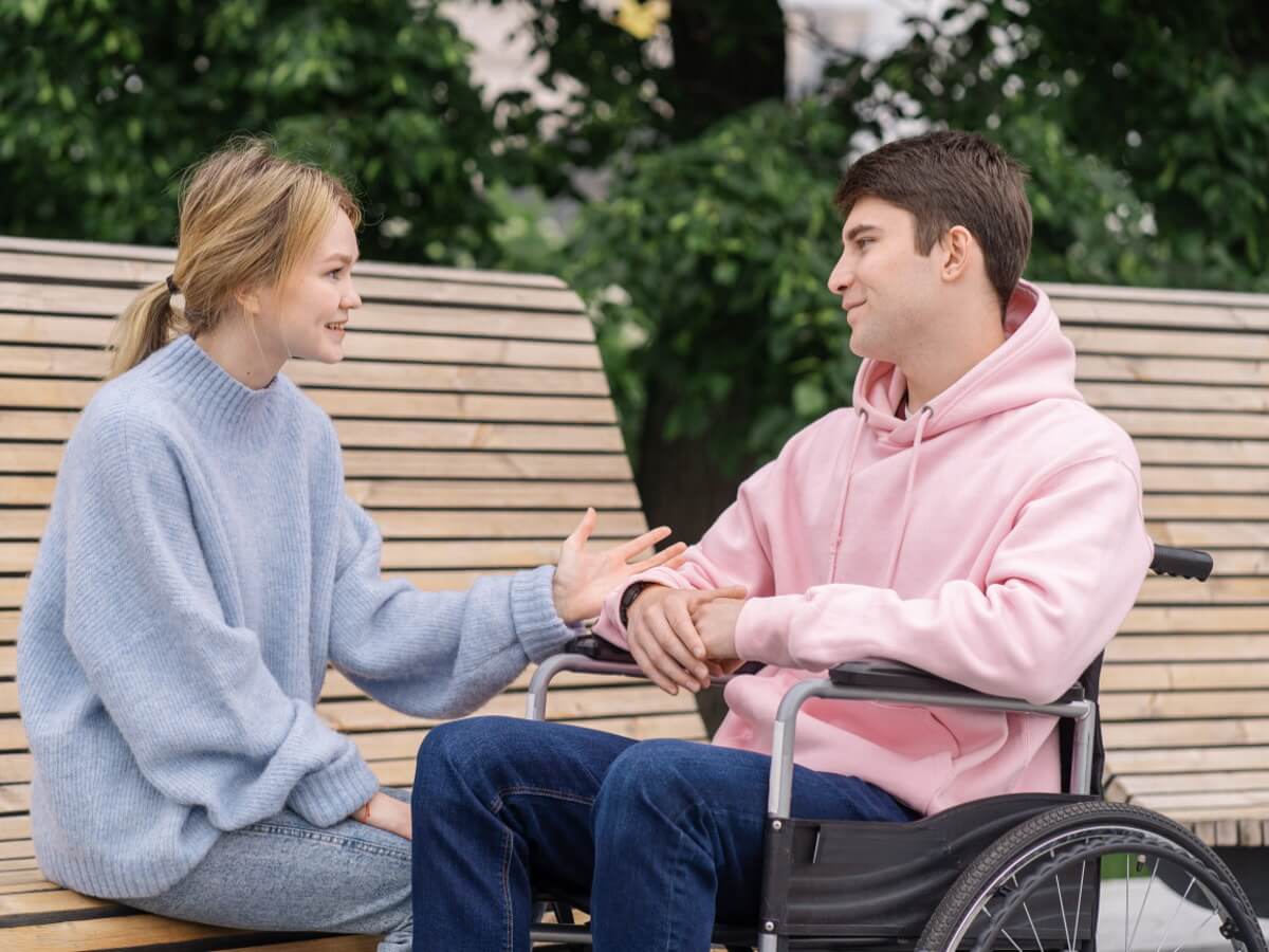 Une jeune femme, assise sur un banc de parc, parle à un jeune homme.