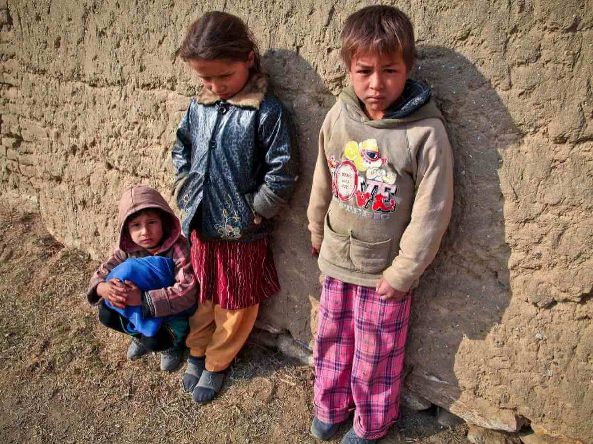 Trois enfants miséreux devant un mur de terre.