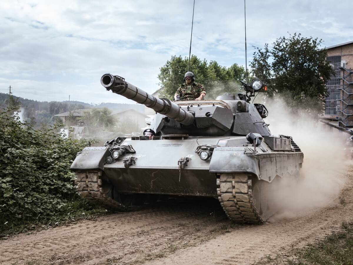 Un tank moderne roule en soulevant de la poussière.