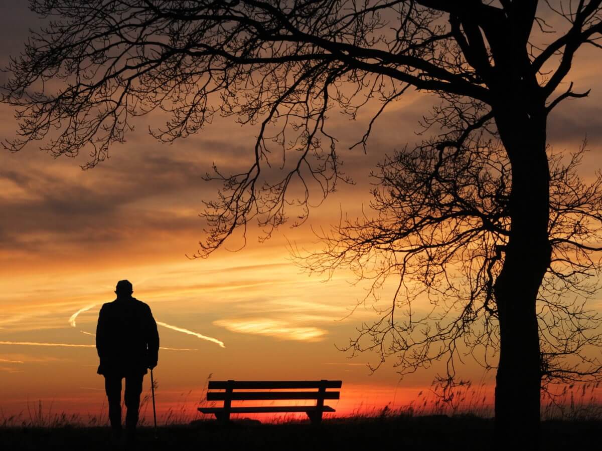 Un vieil homme marche seul devant un coucher de soleil.