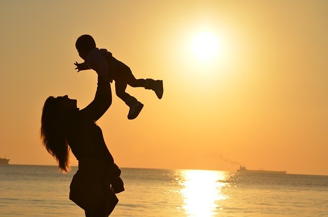 Un bébé dans les bras de sa mère devant le soleil