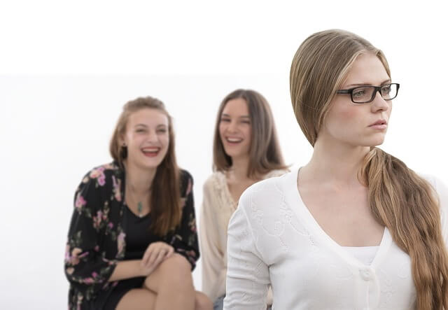 Deux femmes parlent dans le dos d’une troisième.