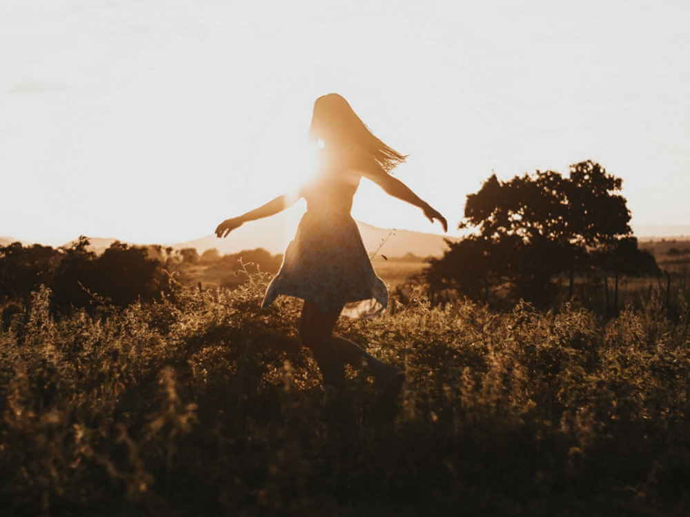 Une jeune femme dance devant le soleil.
