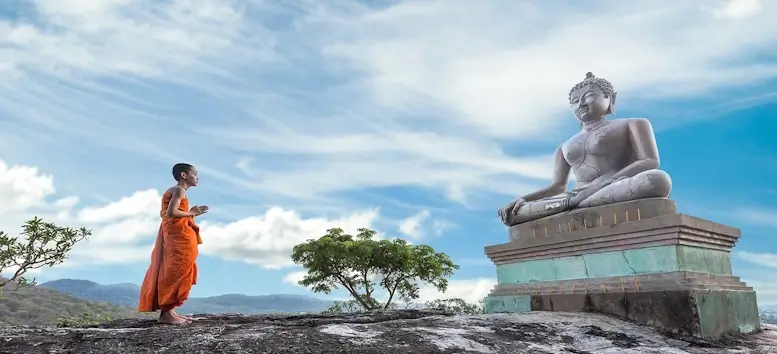 Un jeune moine prit devant une grande statue de Bouddha.