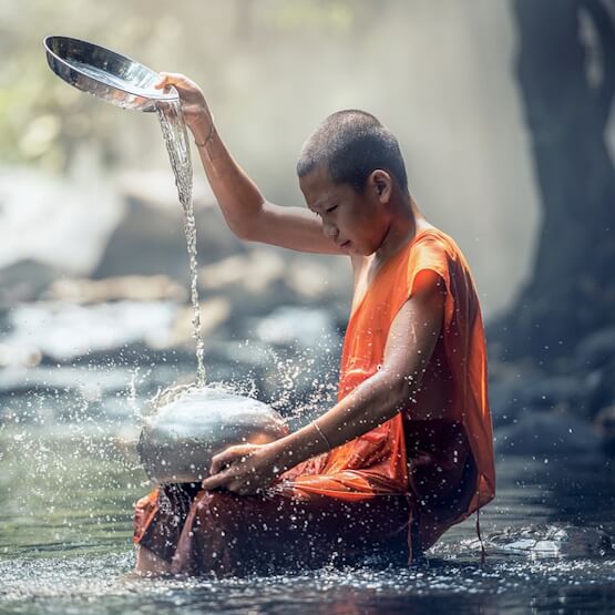 Un jeune moine s'asperge d'eau dans les bois.